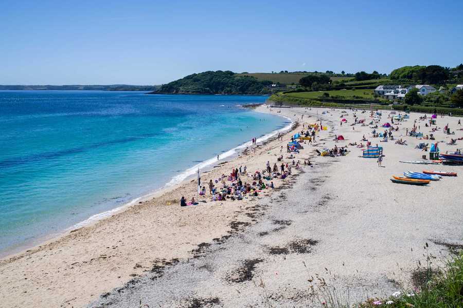 Gyllyngvase beach in Falmouth. The Sea is blue and people are sitting on the white sand.