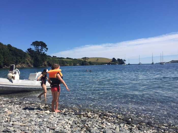 Two small girls and a RIB dinghy on the shore of Grebe Beach on the Helford River, Cornwall