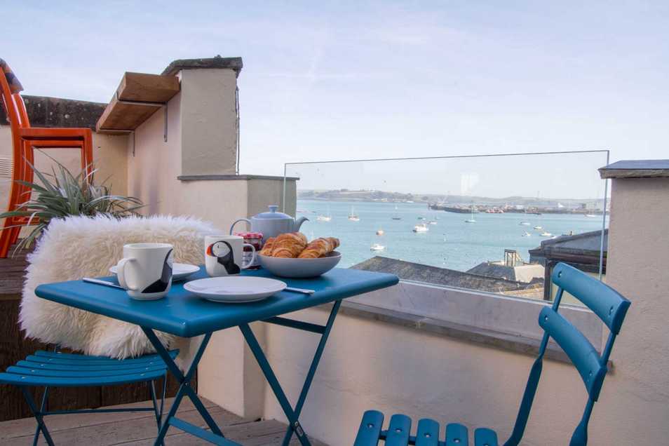 Breakfast set up on the lage patio area of The Brig. A view of Falmouth harbour over the patio dining chairs and table.