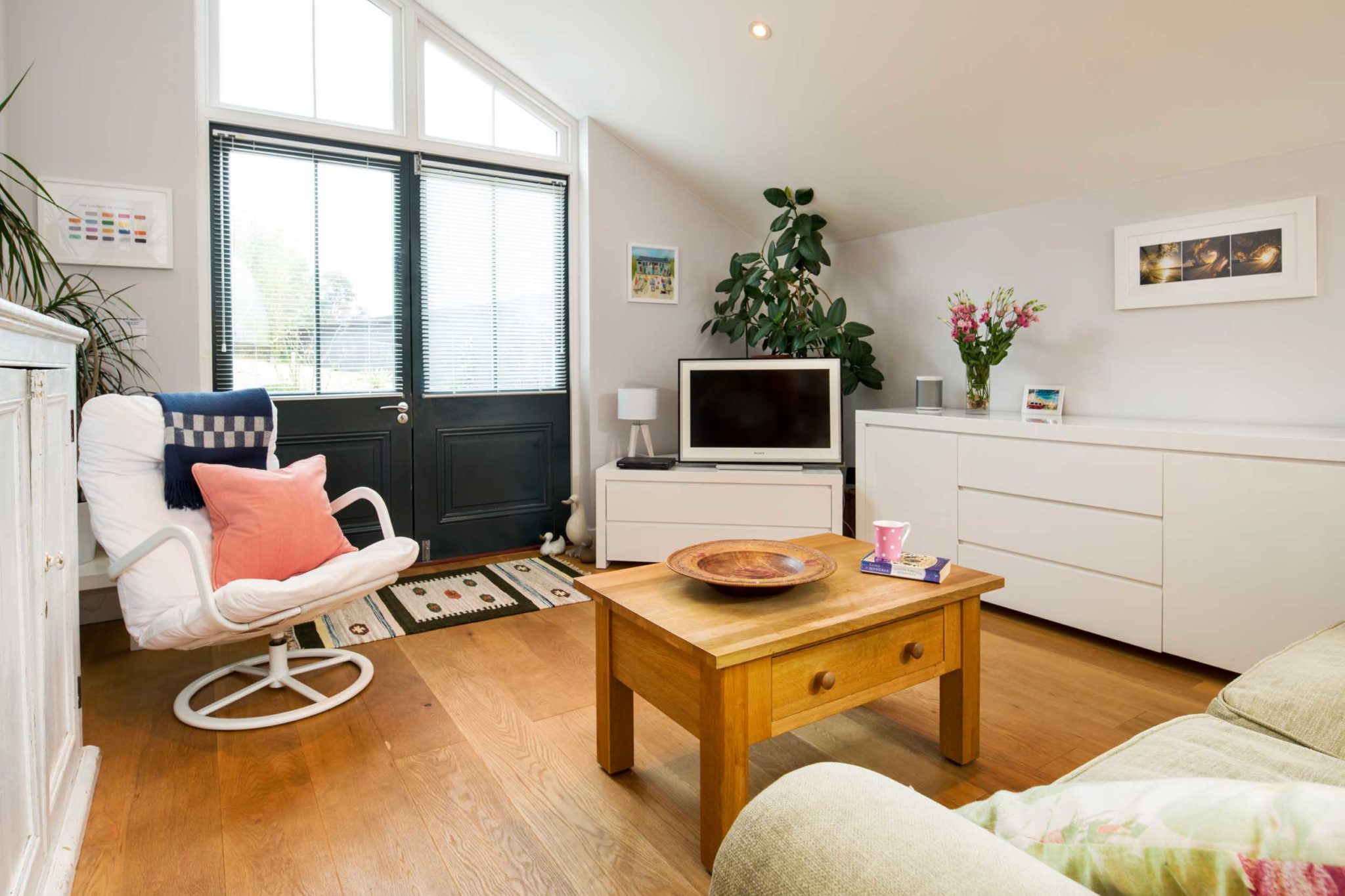 The Living room of The Old School Room in Falmouth. There is a coffee table, comfy seating, and a television. Double doors to the outiside.